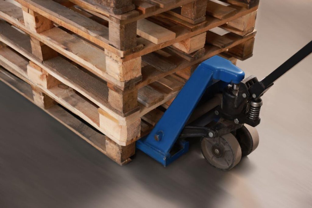 Blue pallet truck transporting wood plates at a construction site, supporting efficient material handling and workflow operations.