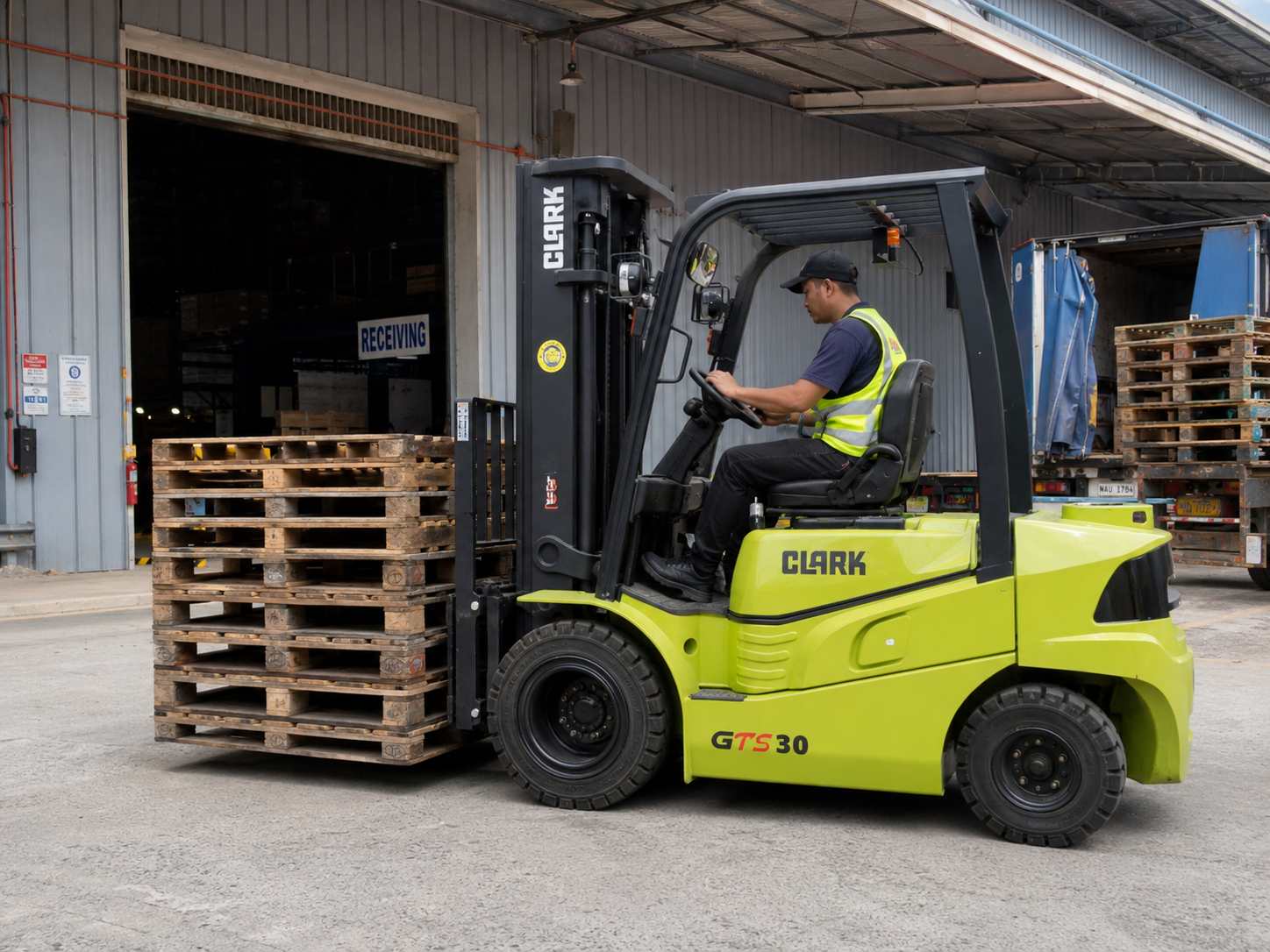 Clark forklift transporting stacked wooden pallets near a receiving dock