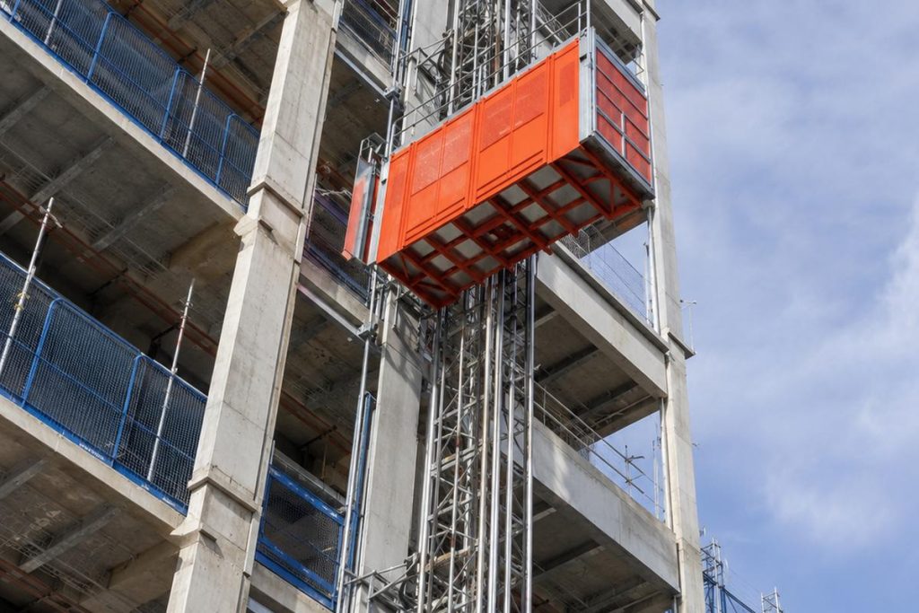 Orange construction hoist operating on high-rise building exterior