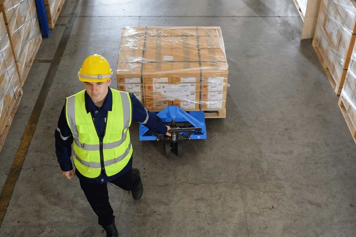 Worker moving a pallet load with a pallet truck to show the physical effort involved in starting pallet movement